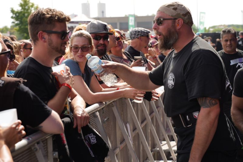 Ein Security-Mitarbeiter verteilt auf dem VAINSTREAM-Festival 2024 (Kingstar Music) an die Gäste der ersten Reihen Wasser aus einer Flasche.