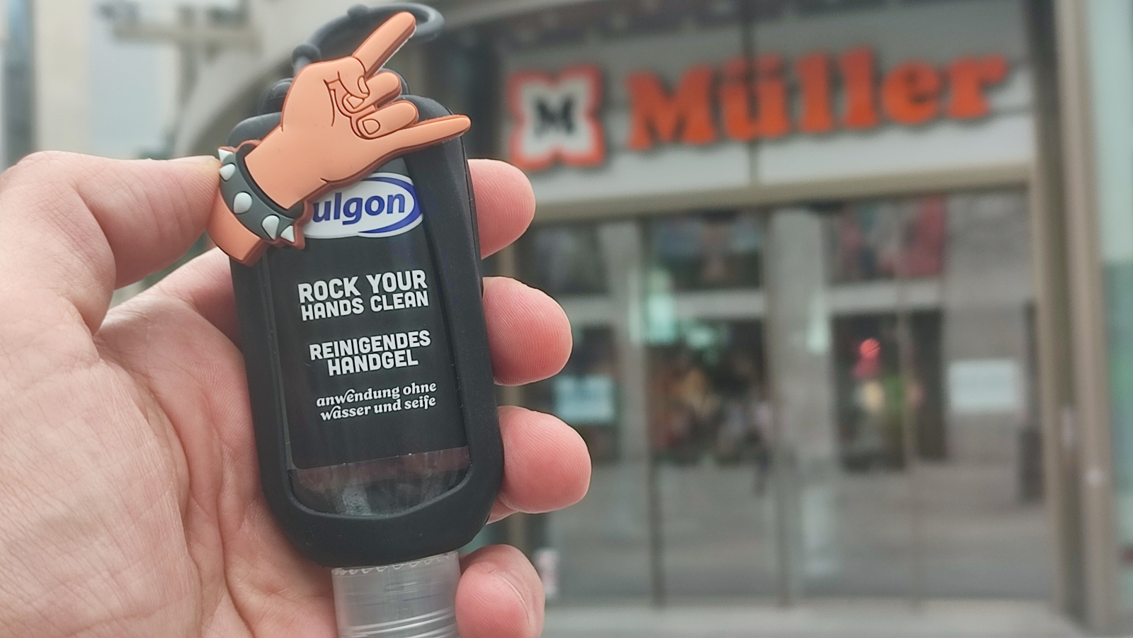 Ein Desinfektionsgel in schwarzer Halterung mit einer gehörnten Hand als Heavy-Metal-Symbol vor einem Müller Drogieriemarkt.