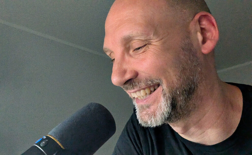 Nahaufnahme eines Mannes, der lächelnd in ein Mikro spricht.
